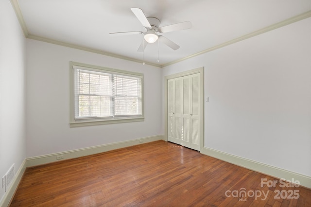 empty room featuring baseboards, wood finished floors, visible vents, and crown molding