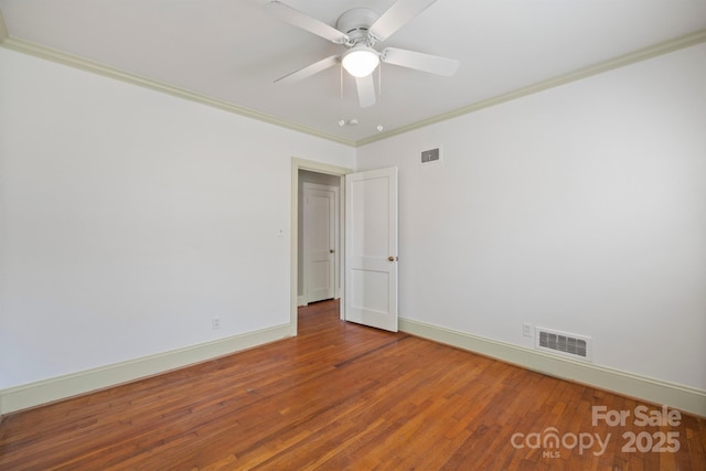 spare room with ornamental molding, wood finished floors, visible vents, and baseboards