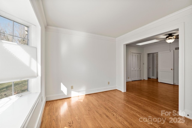 empty room with a ceiling fan, crown molding, light wood-style flooring, and baseboards