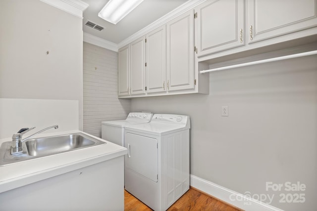 laundry room featuring visible vents, cabinet space, light wood finished floors, washer and clothes dryer, and crown molding