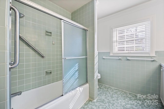 bathroom featuring enclosed tub / shower combo, wainscoting, tile walls, and crown molding