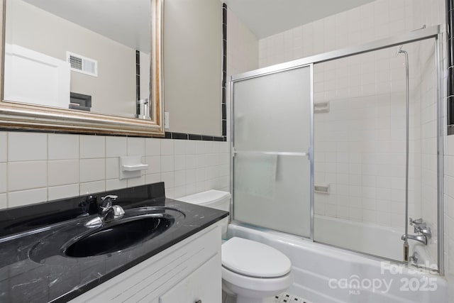 full bathroom with visible vents, toilet, combined bath / shower with glass door, vanity, and tile walls