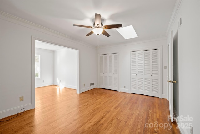 unfurnished bedroom with light wood finished floors, baseboards, ornamental molding, and two closets