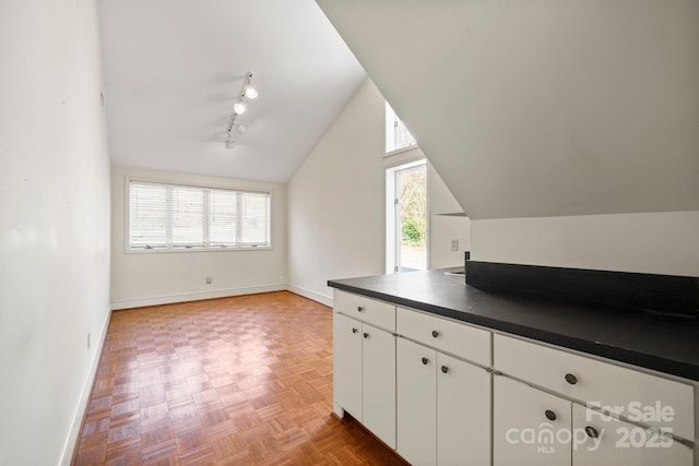 kitchen featuring dark countertops, white cabinets, vaulted ceiling, track lighting, and baseboards