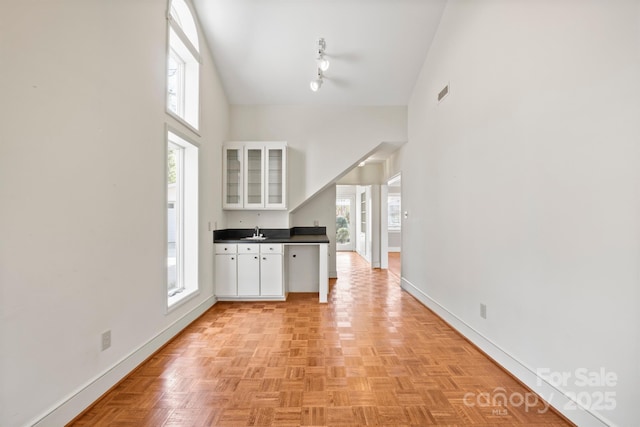 kitchen with dark countertops, a towering ceiling, white cabinetry, and glass insert cabinets