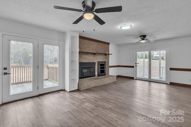 unfurnished living room featuring visible vents, a textured ceiling, a brick fireplace, and wood finished floors