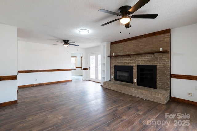 unfurnished living room with a textured ceiling, wood finished floors, a fireplace, baseboards, and ceiling fan