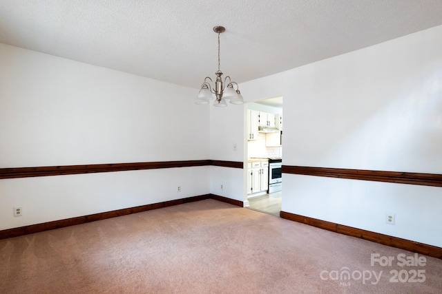 spare room with an inviting chandelier, light colored carpet, baseboards, and a textured ceiling