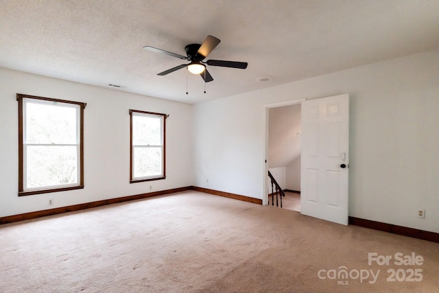 empty room featuring visible vents, baseboards, light colored carpet, a textured ceiling, and a ceiling fan