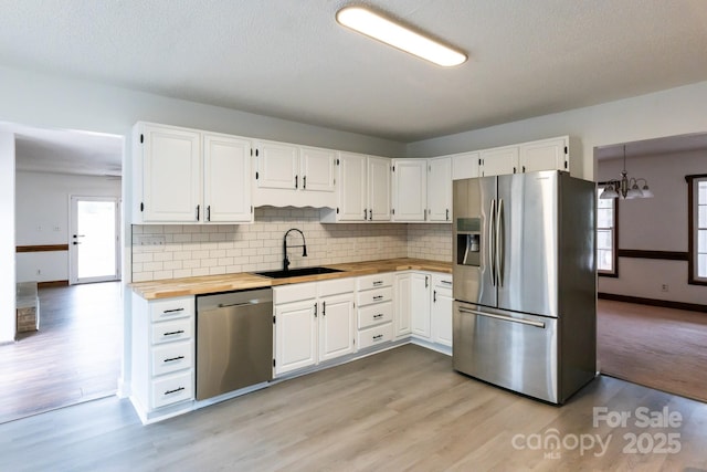 kitchen featuring white cabinets, appliances with stainless steel finishes, butcher block counters, and a sink