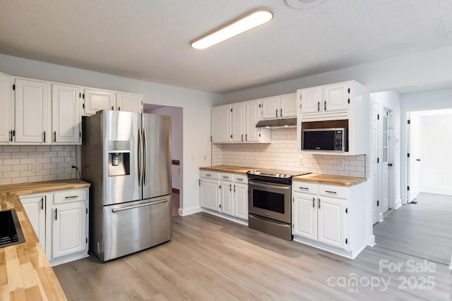 kitchen with under cabinet range hood, stainless steel appliances, butcher block countertops, and white cabinets