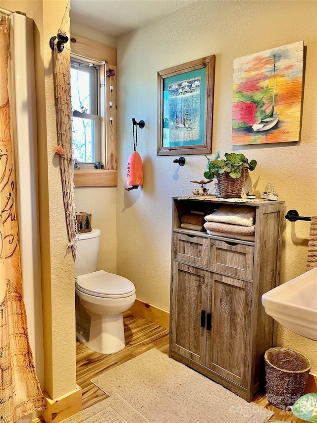 bathroom featuring a textured wall, toilet, wood finished floors, vanity, and baseboards