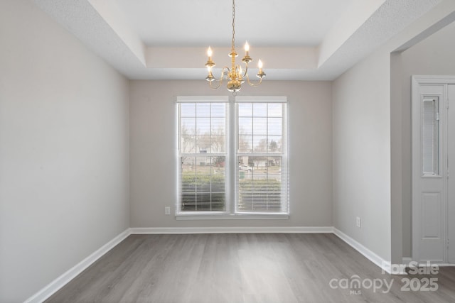 unfurnished dining area with a chandelier, a raised ceiling, baseboards, and wood finished floors