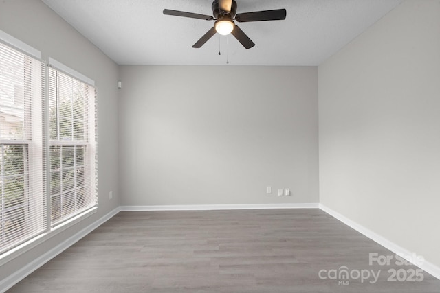 empty room with a textured ceiling, wood finished floors, a ceiling fan, and baseboards