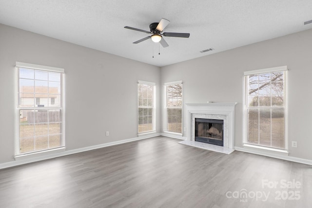 unfurnished living room with a fireplace, plenty of natural light, wood finished floors, and visible vents