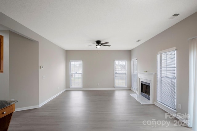 unfurnished living room featuring ceiling fan, a premium fireplace, wood finished floors, and visible vents