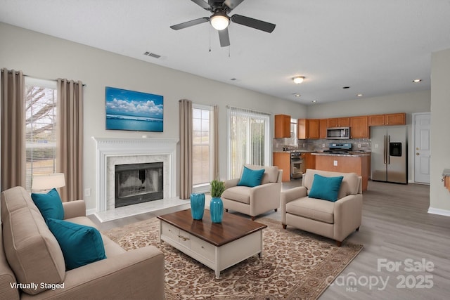 living area with light wood-type flooring, a wealth of natural light, a fireplace, and recessed lighting