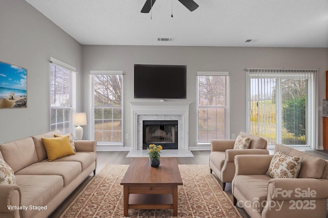 living room with a high end fireplace, a healthy amount of sunlight, visible vents, and wood finished floors