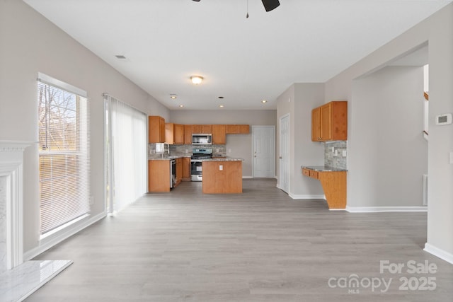 kitchen featuring open floor plan, appliances with stainless steel finishes, brown cabinetry, and decorative backsplash