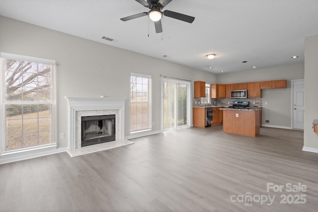 kitchen featuring open floor plan, appliances with stainless steel finishes, brown cabinetry, and decorative backsplash