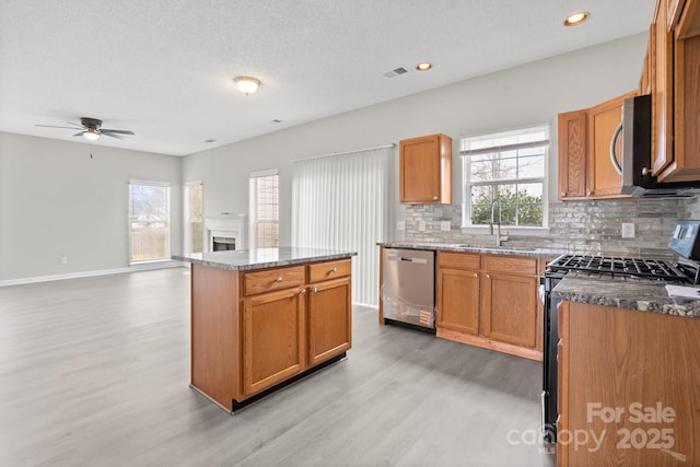 kitchen with decorative backsplash, light wood-style flooring, stainless steel appliances, a fireplace, and a sink