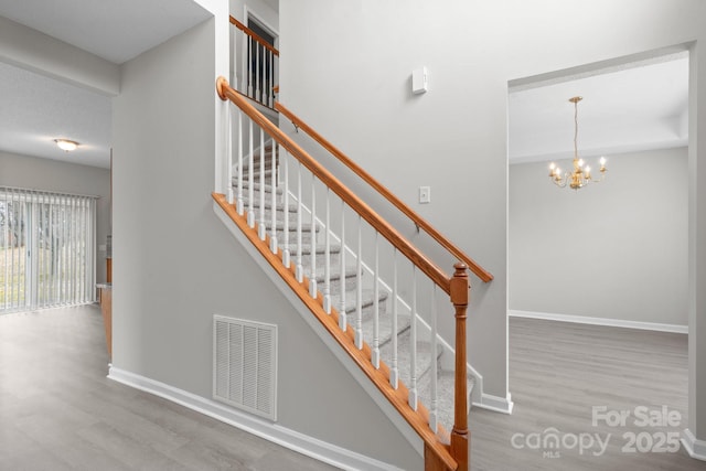 stairs with an inviting chandelier, wood finished floors, visible vents, and baseboards