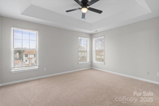 carpeted spare room featuring baseboards, a tray ceiling, and a ceiling fan