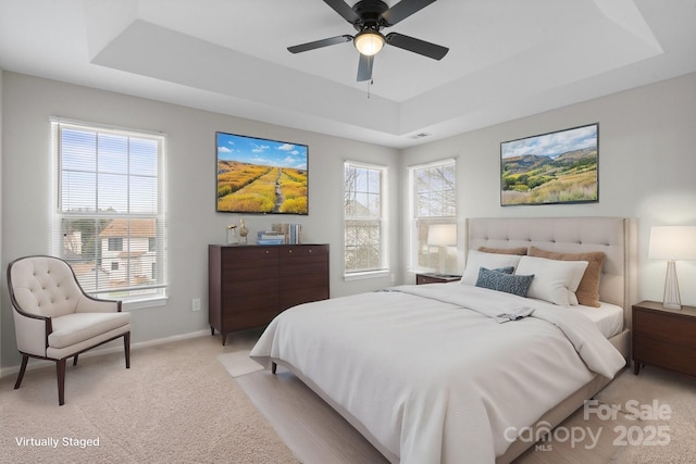 bedroom with a ceiling fan, a tray ceiling, light colored carpet, and baseboards