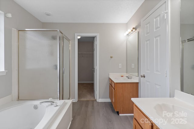 bathroom with a textured ceiling, a garden tub, wood finished floors, two vanities, and a shower stall