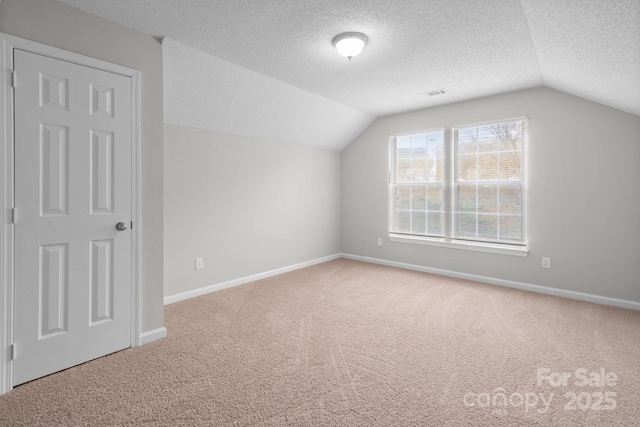 additional living space with carpet floors, baseboards, vaulted ceiling, and a textured ceiling