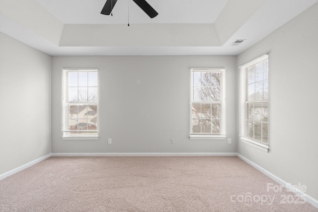 empty room with plenty of natural light, a raised ceiling, and visible vents