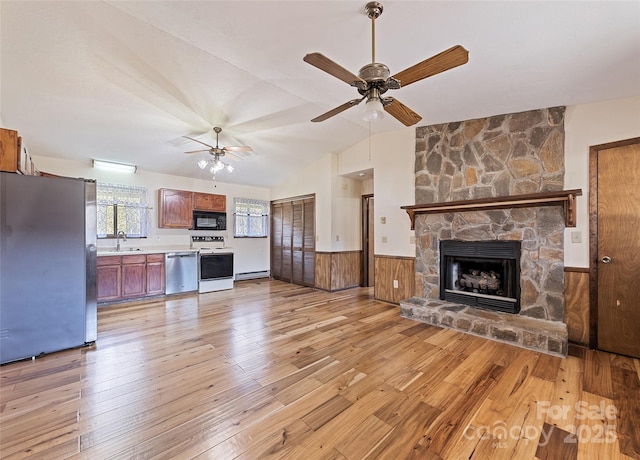 unfurnished living room featuring light wood finished floors, a wainscoted wall, vaulted ceiling, a stone fireplace, and a sink