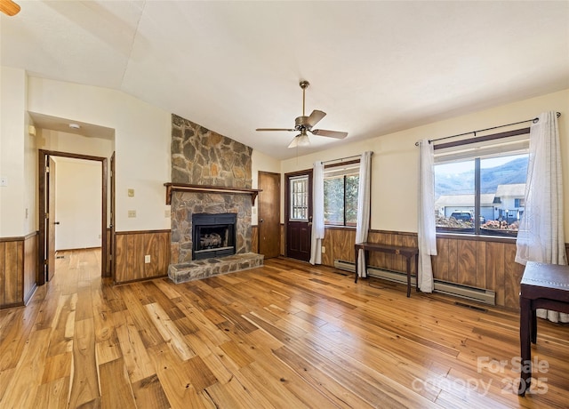 unfurnished living room featuring a wainscoted wall, a stone fireplace, vaulted ceiling, and light wood-style floors