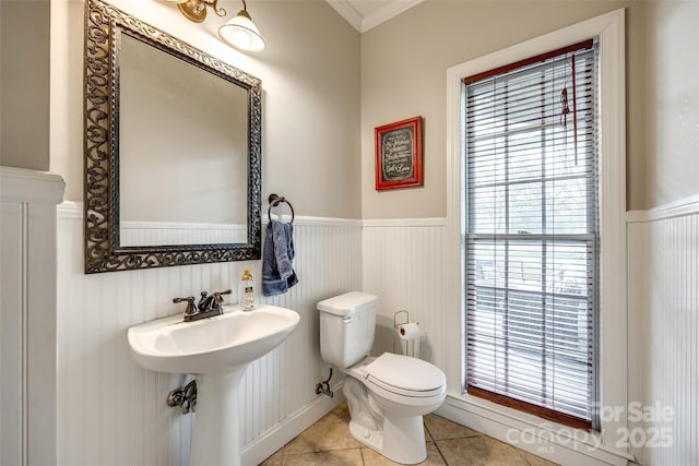 half bathroom with toilet, a wainscoted wall, plenty of natural light, and tile patterned floors