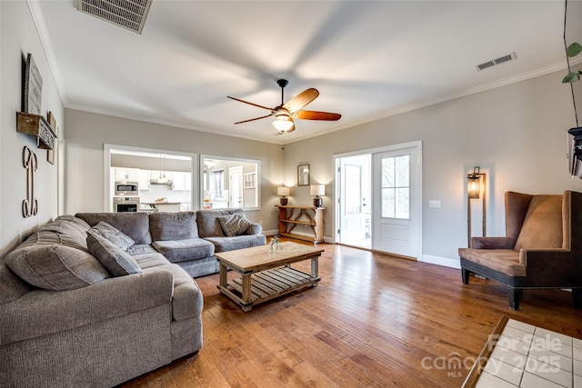 living area with light wood-style floors, visible vents, and ornamental molding