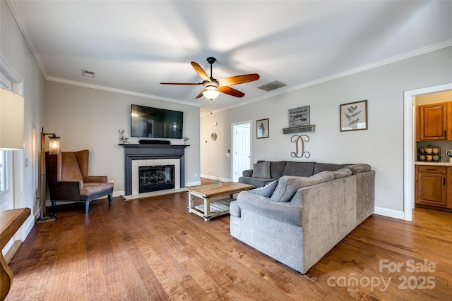 living area featuring a tile fireplace, visible vents, crown molding, and hardwood / wood-style flooring