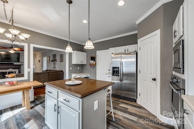 kitchen with dark wood-style floors, stainless steel appliances, ornamental molding, white cabinetry, and a kitchen island