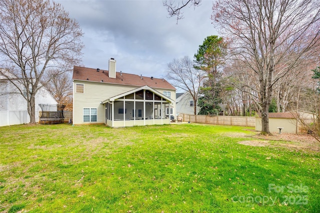 back of house featuring a sunroom, a fenced backyard, a chimney, and a yard