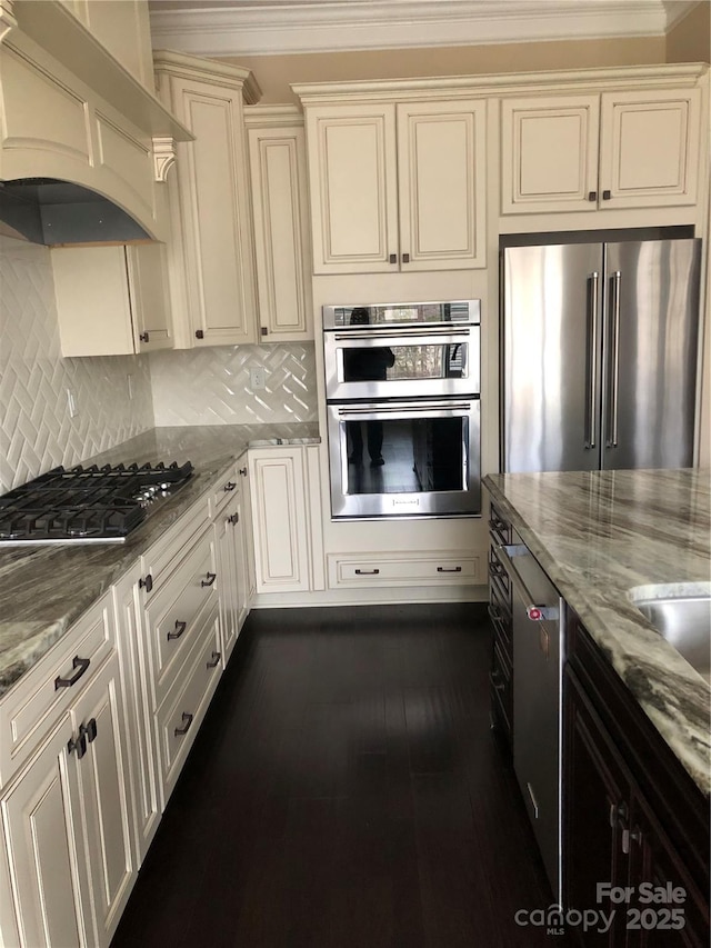 kitchen featuring tasteful backsplash, custom range hood, appliances with stainless steel finishes, light stone counters, and cream cabinets