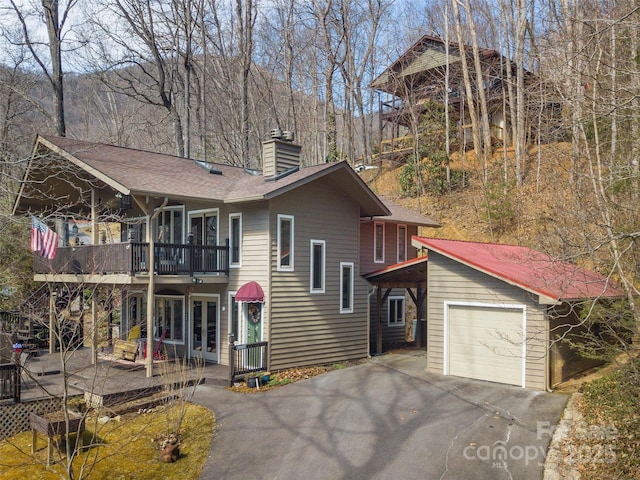 view of front of home featuring french doors, a chimney, an attached garage, a deck, and driveway