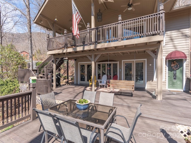 wooden terrace featuring ceiling fan, french doors, outdoor dining area, and stairway