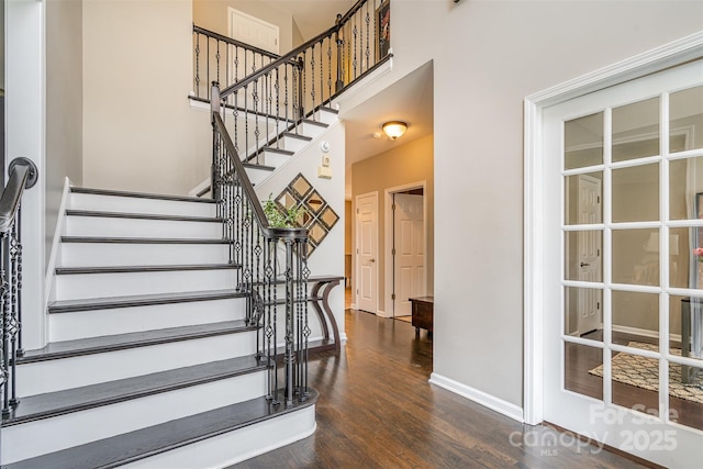 stairway featuring a high ceiling, baseboards, and wood finished floors