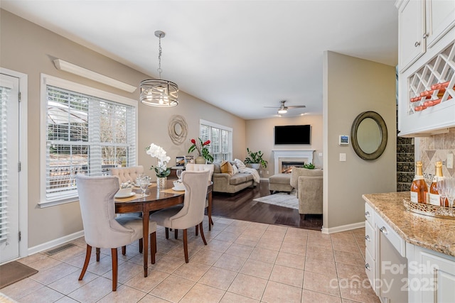 dining area with light tile patterned flooring, a glass covered fireplace, a ceiling fan, and baseboards