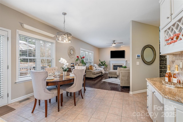 dining room with light tile patterned floors, ceiling fan, baseboards, and a glass covered fireplace