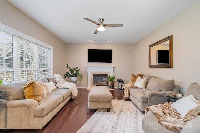 living room featuring a ceiling fan, a glass covered fireplace, baseboards, and wood finished floors