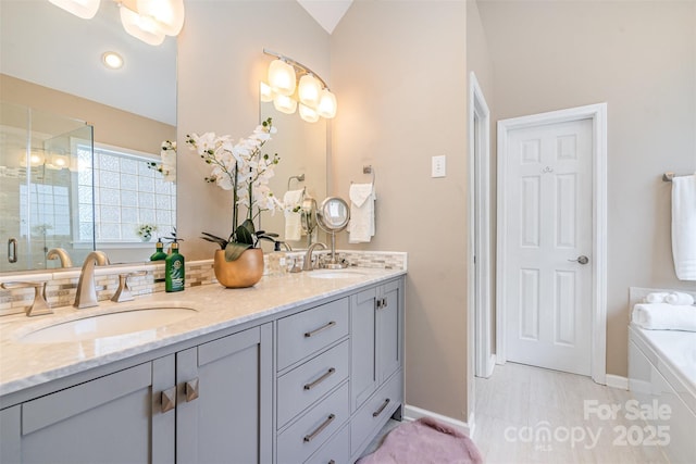 bathroom featuring double vanity, a stall shower, a bathtub, and a sink