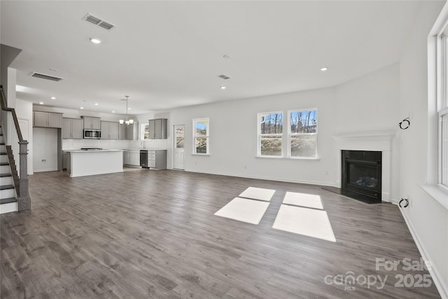 unfurnished living room featuring dark wood-style floors, stairway, a fireplace with flush hearth, and visible vents