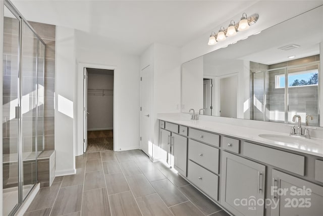 full bathroom with a sink, double vanity, a stall shower, and a walk in closet