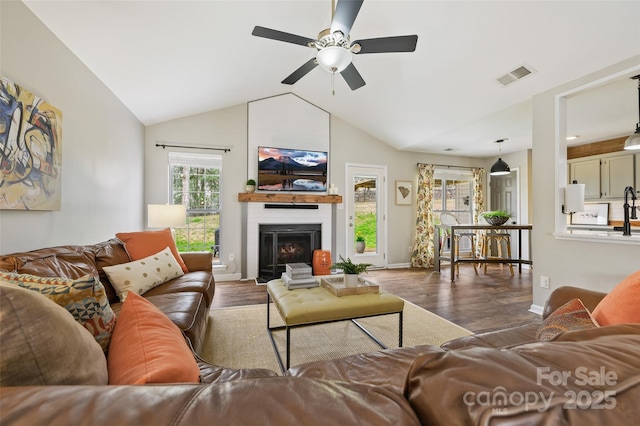 living room with baseboards, visible vents, a glass covered fireplace, lofted ceiling, and wood finished floors