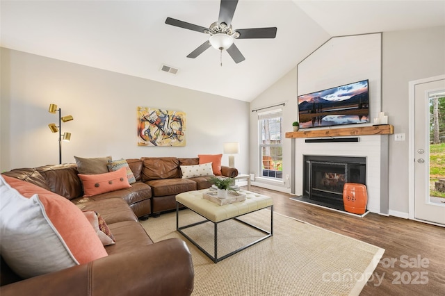 living room with lofted ceiling, visible vents, a glass covered fireplace, a healthy amount of sunlight, and wood finished floors